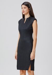 Robe noire sans manches avec un col montant, coupe ajustée, fentes sur les côtés et texture lisse. Fabriquée en tissu structuré avec une finition mate.