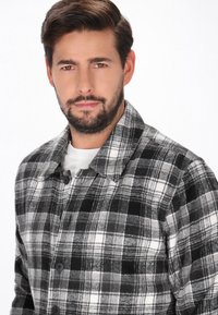 Mustavalkoinen ruudullinen takki pehmeästä, teksturoidusta kankaasta, jossa on kaulus, edessä napit ja rento istuvuus.