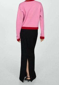 Maglione rosa con dettagli rossi, abbinato a una gonna nera con uno spacco laterale. L'outfit presenta una silhouette rilassata e una texture morbida.