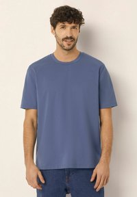 Modré tričko s krátkým rukávem a kulatým výstřihem, uvolněného střihu, vyrobené z hladkého materiálu, v kombinaci s denimovými džínami.