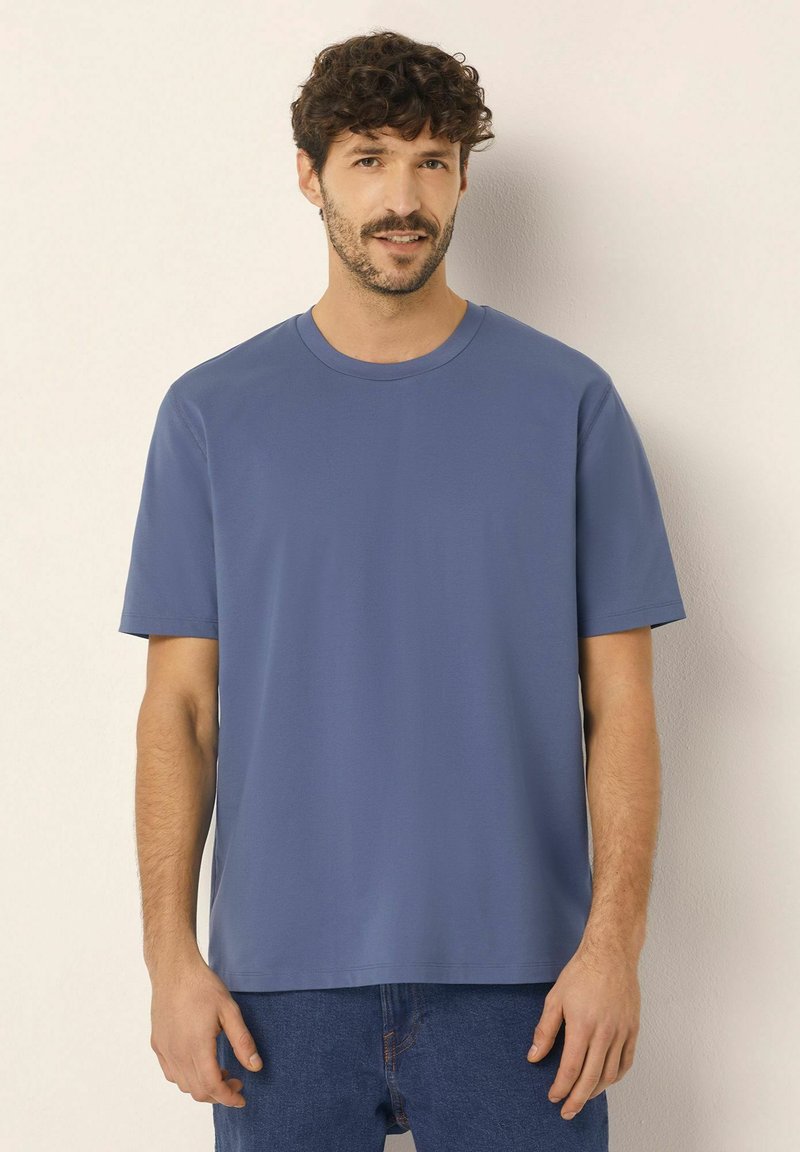 Modré tričko s krátkým rukávem a kulatým výstřihem, uvolněného střihu, vyrobené z hladkého materiálu, v kombinaci s denimovými džínami.