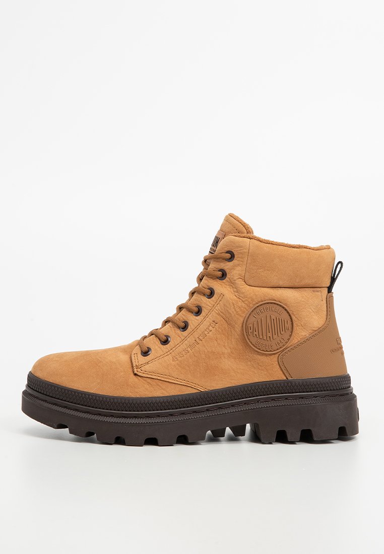 Tan-farbene Wildleder-Ankle-Boots mit runder Spitze, schwarzer Gummisohle, sechs Metallösen und kreisförmigem Logopatch an der Seite. Texturiertes Obermaterial und gepolsterter Schaft.