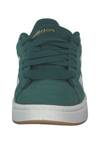 Gröna mockaskor med vita detaljer, platta snören och gyllene logotyp på tungan. Har en vit mellansula och en tan gummisula.