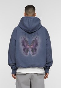 Navy blue hoodie with oversized fit, featuring a large purple butterfly graphic on the back and the word "gonzales" above it.