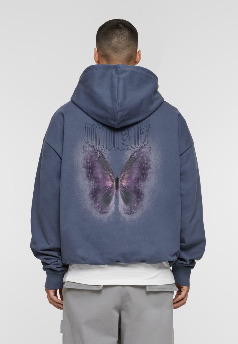 Sudadera azul marino de corte oversize, con un gran gráfico de una mariposa morada en la parte posterior y la palabra "gonzales" encima.