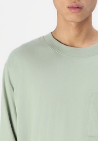 Langarmshirt van lichtgroene katoen. Crew neck ontwerp met een borstzak. Gladde textuur, ontspannen pasvorm en gestikte details rondom de randen.