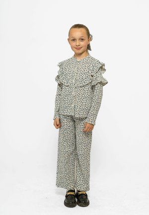 Completo a due pezzi con stampa floreale, caratterizzato da colletto arricciato e maniche lunghe, in crema chiaro con fiori blu; pantaloni a gamba larga e scarpe nere.