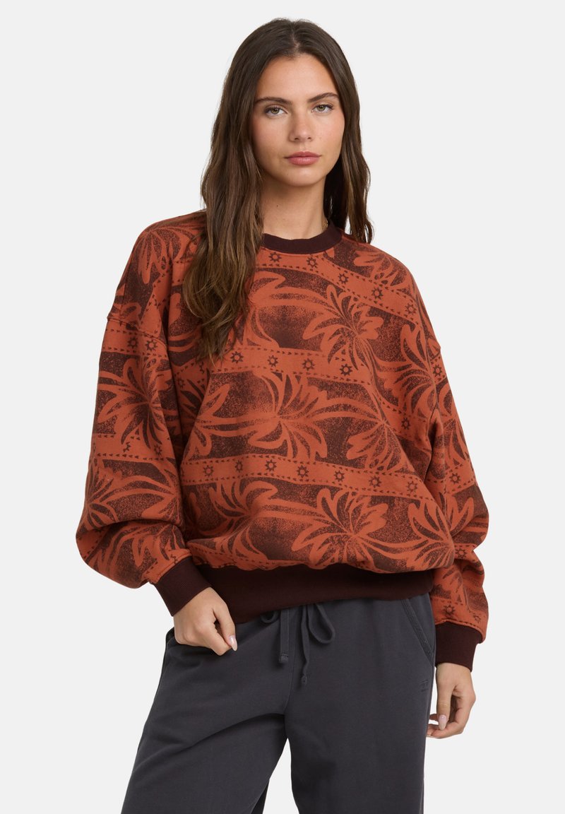 Czerwony sweter z długim rękawem w wzory, z kwiatowym motywem oraz ściągaczami przy mankietach i dekolcie. W połączeniu z ciemnoszarymi spodniami.