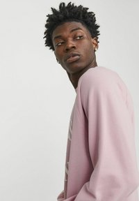 Sudadera rosa claro de tela suave, con cuello redondo y mangas largas. En la parte frontal presenta un diseño de texto en contraste.