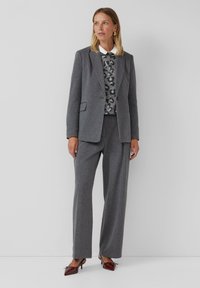 Grijze pinstripe pak met een op maat gemaakt jasje en wijde broekspijpen. Gelaagd over een gestreept grijs vest, gecombineerd met bordeauxrode hakken.