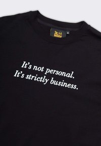 T-shirt in cotone nero con scollo tondo, caratterizzato da testo bianco che recita "Non è personale. È solo affari." in un carattere moderno.