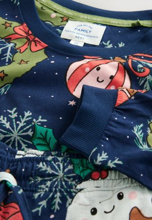 Marinblå pyjamas set med festliga mönster, inklusive dekorationer och snöflingor, med ribbade muddar och mjukt tyg. Etikett synlig.