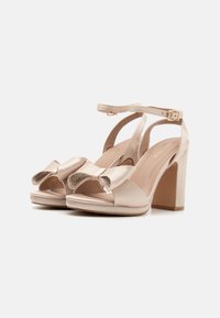 Beige satin högklackade sandaler med en bred rosettdetalj och glittrande accenter. Har en ankelrem och en blockklack för stabilitet.