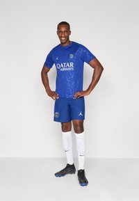 Blå atletisk kortærmet trøje med Qatar Airways logo, parret med matchende shorts. Funktioner inkluderer hvide accenter og ribbet tekstur.