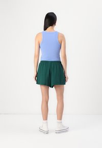 Canotta a coste blu chiaro abbinata a pantaloni corti verdi ampi. Sneakers alte bianche con cuciture visibili e suole testurizzate.