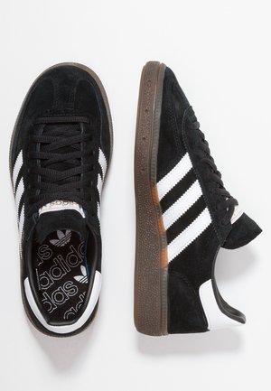 Schwarze Adidas-Sneaker mit weißen Streifen, braunen strukturierten Sohlen und schwarzen Schnürsenkeln, von oben und seitlich vor weißem Hintergrund gezeigt.