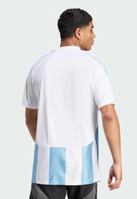 Maillot de sport blanc avec des rayures verticales bleu clair sur les côtés et le dos. Fabriqué en tissu lisse et respirant avec une coupe décontractée.