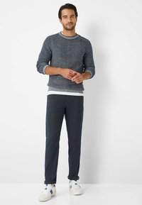Gebreide blauwe trui met ribbelstructuur en grijze ronde hals, gecombineerd met donkergrijze broek en witte sneakers met blauwe accenten.