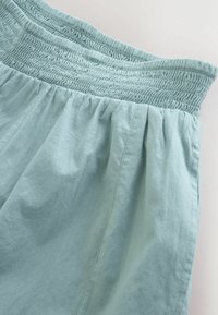 Tissu bleu clair avec taille élastique froncée et coutures verticales visibles, montrant la texture et les plis.