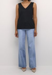 Sort ærmeløs v-hals top, parret med lyseblå flarejeans og beige hæle, med et glat stof og en afslappet pasform.