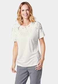 Witte korte mouwen t-shirt met kantdetails op de schouders, ronde halslijn en een zachte textuur, gecombineerd met zwart-witte geblokte broek.