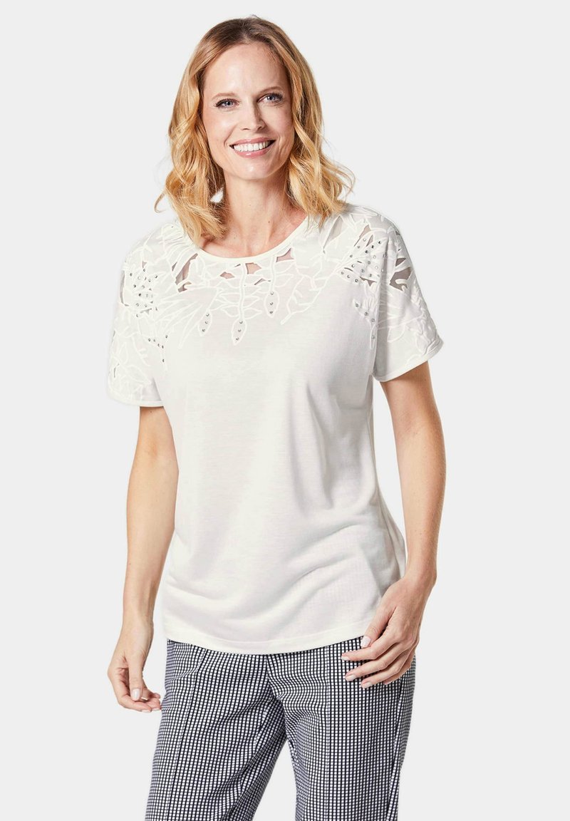 Witte korte mouwen t-shirt met kantdetails op de schouders, ronde halslijn en een zachte textuur, gecombineerd met zwart-witte geblokte broek.