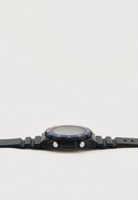 Čierne analógové hodinky s drsným silikónovým remienkom, okrúhlym ciferníkom a modro-červeným rámčekom. Na boku sa nachádzajú dve strieborné tlačidlá.