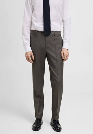 Pantaloni da donna grigi su misura realizzati in tessuto testurizzato, caratterizzati da una vestibilità slim, passanti per cintura e una classica piega frontale, abbinati a scarpe nere.
