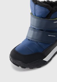 Botte d'hiver bleue pour enfant avec semelle en caoutchouc noir, bandes Velcro, doublure en polaire et étiquette imperméable Amphibiox sur un fond blanc.