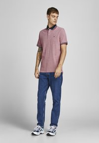 Rød tekstureret polo skjorte med marineblå krave og hvid-røde stribede ærmer, parret med blå denim jeans og sorte sportsko.
