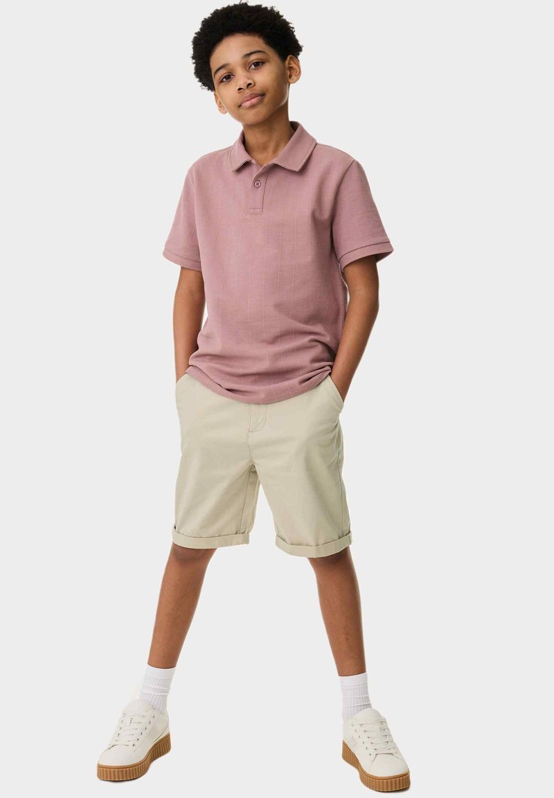 Ljusrosa polo-skjorta med korta ärmar och strukturerat mönster, kombinerad med beigefärgade knälånga shorts och vita sneakers med gummisula.