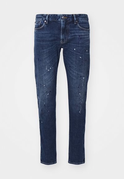 Dark blue denim jeans with a slim fit, featuring paint splatters, visible stitching, and standard five-pocket design. Straight leg cut.
