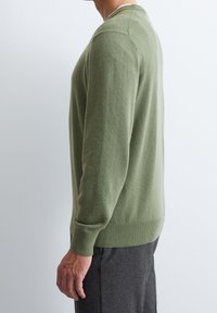 Groene gebreide trui met lange mouwen, ronde hals, ribgebreide manchetten en zoom. Zachte textuur, slim fit silhouet, gedragen met donkere broek.