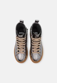 Zapatillas deportivas altas de color gris metálico con cordones beige y suela de goma marrón. Cuentan con un cierre de cremallera y un tobillo acolchado para mayor comodidad.