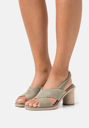 Sandales à talons en daim vert avec un design à brides croisées, bout ouvert et un talon tissé texturé. Un tissu doux autour du talon apporte du confort.