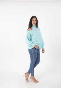 Maglione lavorato a maglia azzurro chiaro con colletto alto e spalle scoperte, abbinato a jeans aderenti e sandali trasparenti con tacco alto.