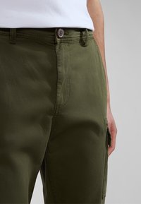 Olivově zelené cargo kalhoty s úzkým střihem, vybavené knoflíkovým zapínáním a bočními kapsami. Tkanina se zdá být lehká s hladkým povrchem.