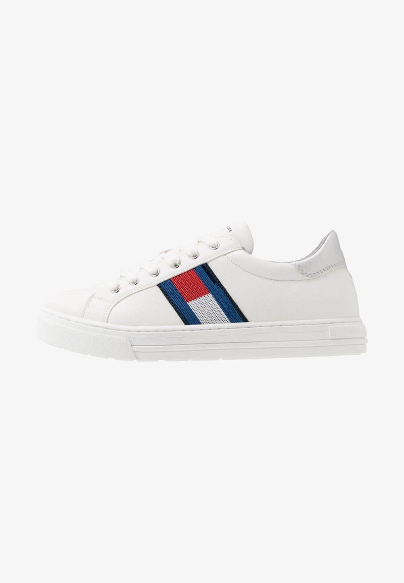 Baskets basses blanches avec fermeture à lacets à l’avant et détail en tissu rayé rouge, blanc et bleu sur le côté.