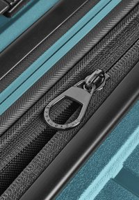 Primo piano di una tirazip in metallo su una cerniera in tessuto nero attaccata a una valigia blu con texture.
