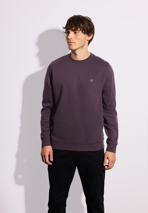 Lila Sweatshirt mit Rundhalsausschnitt, gerippten Bündchen und einem kleinen Logo-Druck auf der Brust, kombiniert mit schwarzen Hosen. Weicher Stoff, lässige Passform.