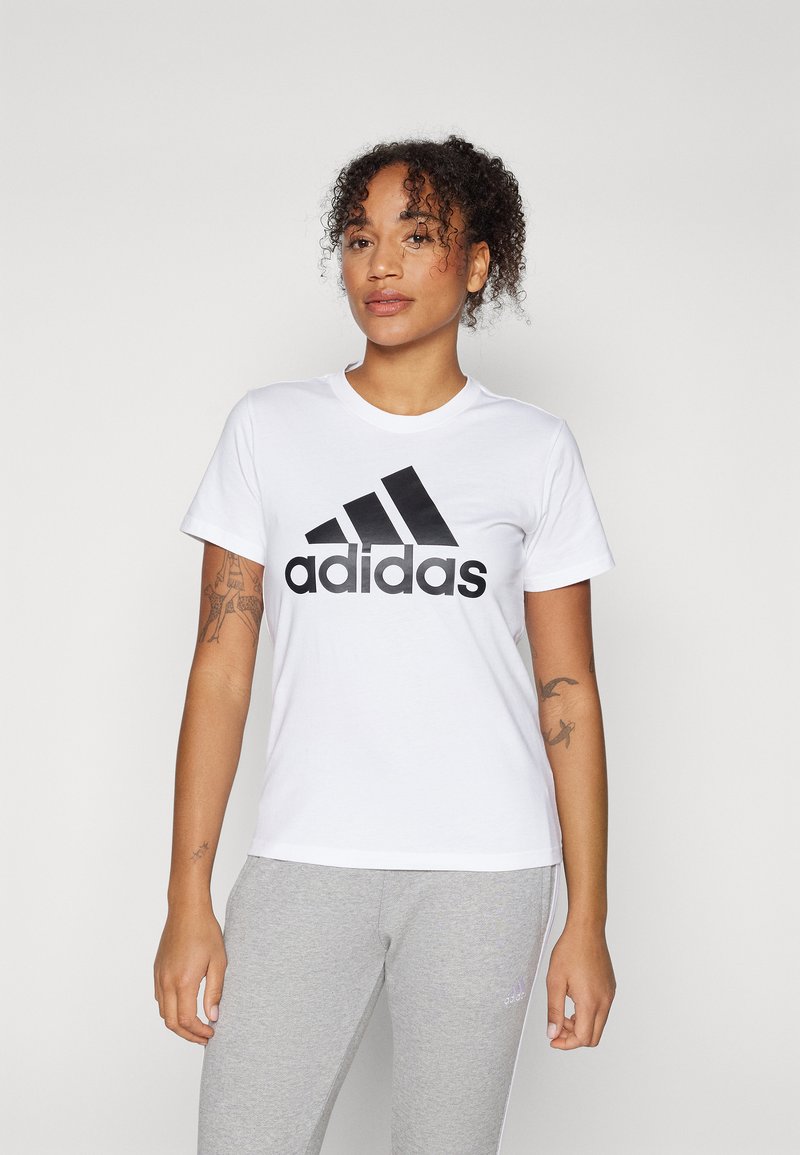 Hvit bomull T-skjorte med en stor svart Adidas-logo. Har korte ermer og rund hals. Kombinert med grå joggebukser.