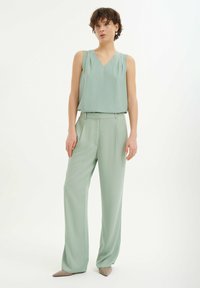 Jasnozielony bezrękawnik z dekoltem w serek i plisami, w zestawie z dopasowanymi spodniami o szerokich nogawkach. Gładki materiał o miękkiej teksturze.