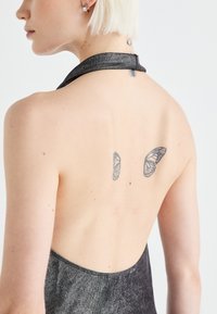 Sort halterneck kjole med metalisk glans, der har en åben ryg. To sommerfuglstatuer er synlige på den øverste ryg.