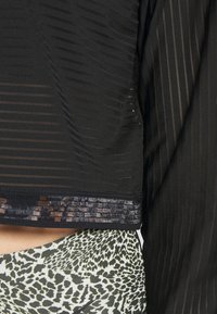 Top nero trasparente con righe verticali, caratterizzato da un orlo testurizzato e un motivo a contrasto sul capo inferiore. Materiale morbido e leggero.