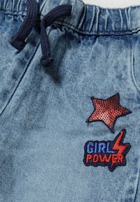 Denim kratke hlače s svetlo modrim finišem, ki imajo teksturirano površino, mornarsko modro vrvico in rdeče ter modre vezenine, vključno z zvezdo in "GIRL POWER".