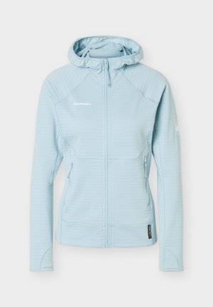 Ανοιχτό γαλάζιο μπουφάν με φερμουάρ και κουκούλα, μακριά μανίκια, πλαϊνές τσέπες με φερμουάρ και λογότυπο Mammut στο στήθος και στο αριστερό χέρι.