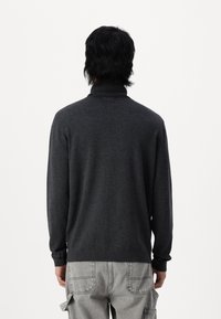Mørkegrå sweater med høj krave, ribbede manchetter og kant. Blød tekstur, tætsiddende silhuet, ingen mønstre eller bemærkelsesværdige metaldele synlige.