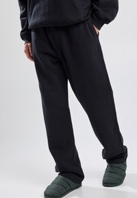 Pantalones de chándal negros con un ajuste relajado, hechos de material suave, con una cinturilla elástica y un pequeño parche de logo en el costado.