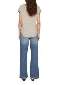 Beige kortärmad topp med rundad nederkant, kombinerad med vida blå denimjeans med fransade kanter och en blekt tvätt.