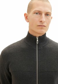 Szary sweter na zamek z prążkowaną fakturą i wysokim kołnierzem. Posiada srebrny zamek i poziome paski w okolicy klatki piersiowej.